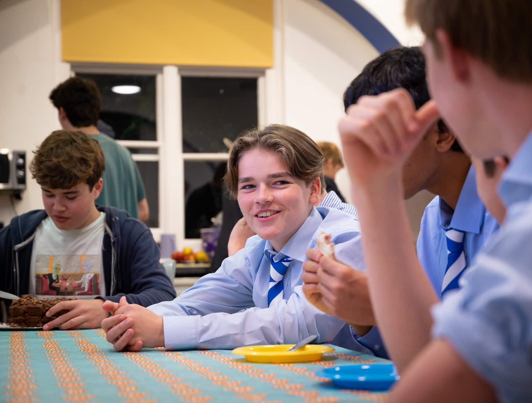 Boy sat eating and drinking with his friends in shirt and tie