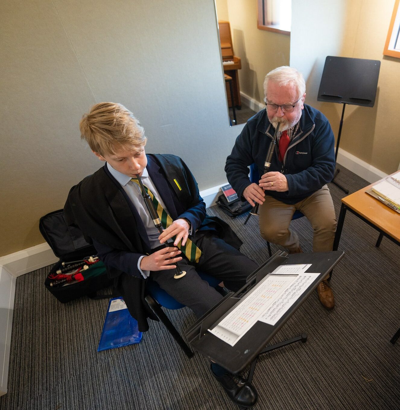 Boy has bagpipes lesson with male teacher in a small room with piano