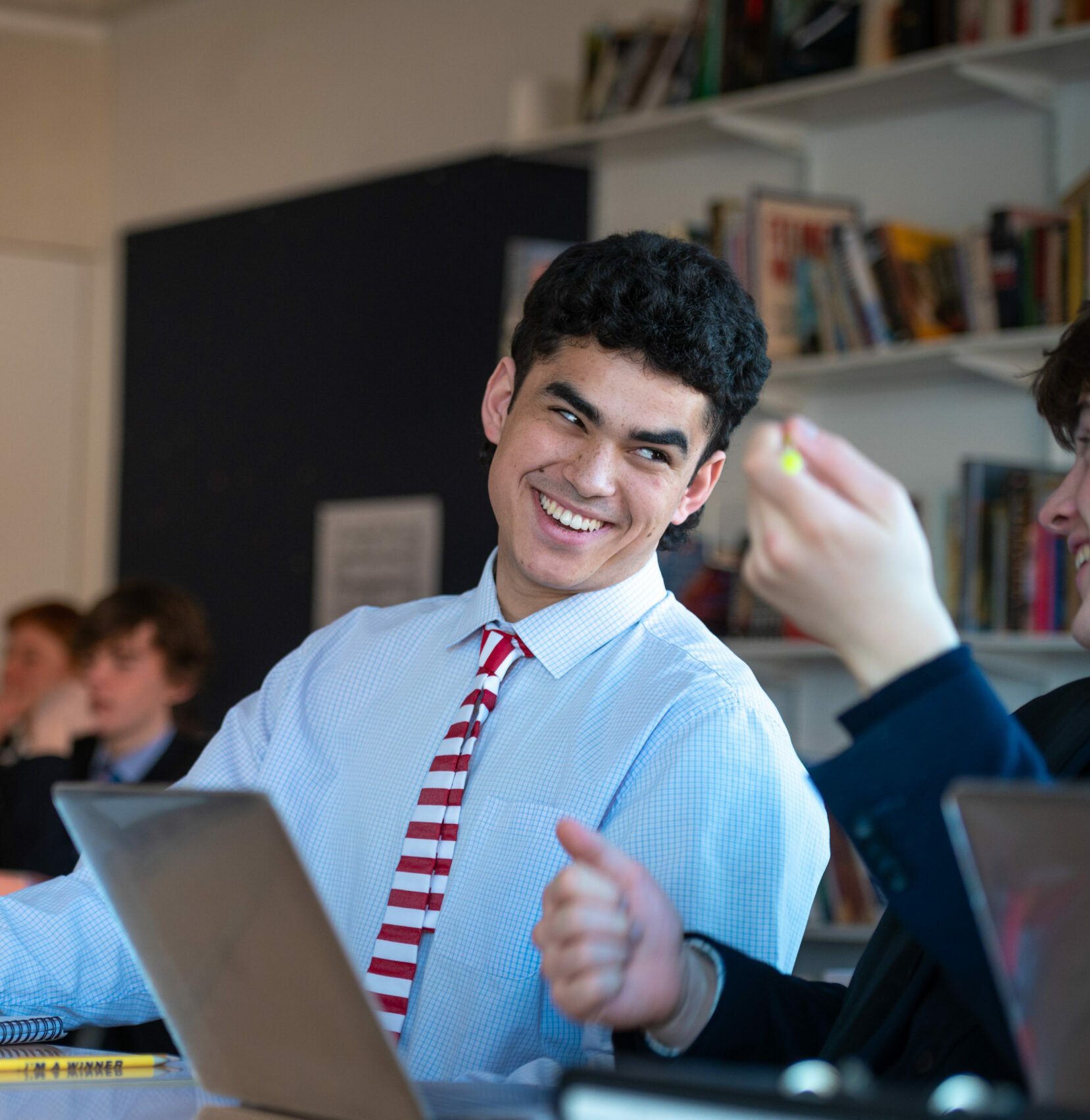 Boy sat in a classroom talking to a friend wearing shirt and tie