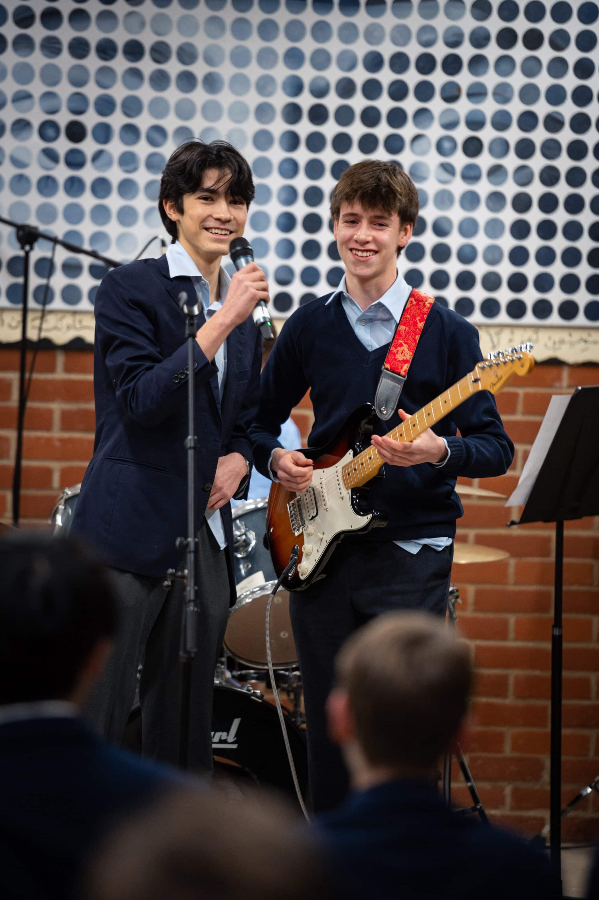 Boy plays electric guitar whilst sat down in a modern building