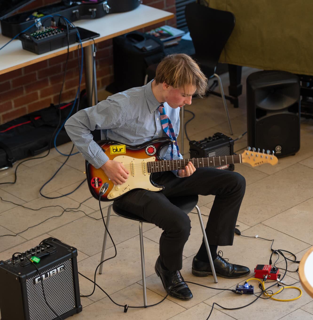 Boy plays electric guitar whilst sat down in a modern building