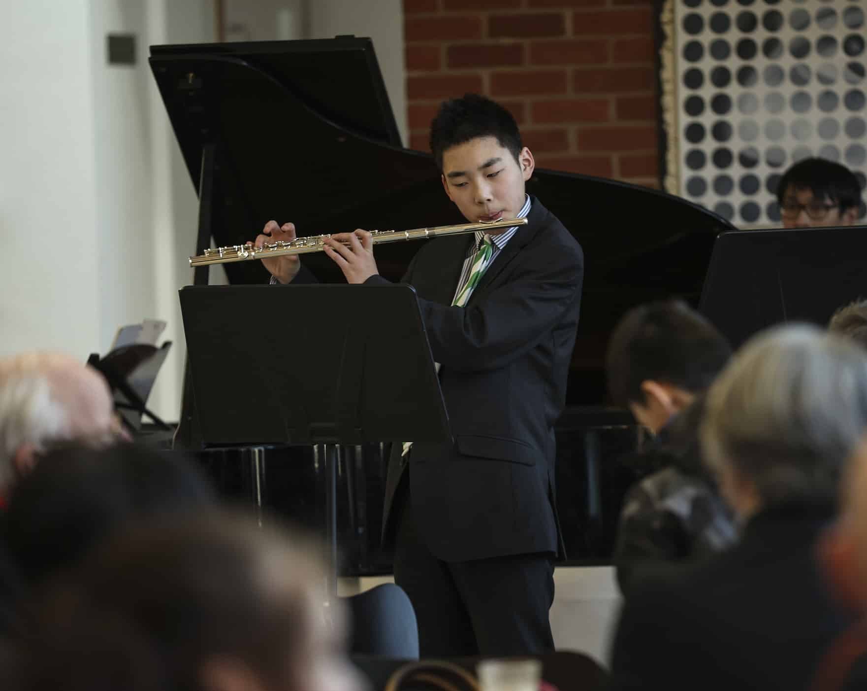 Boy plays the flute in a concert with grand piano in the background