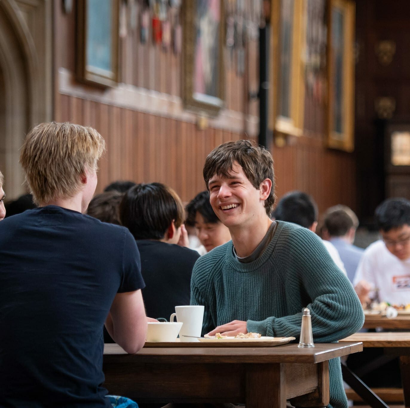 Boy eating in a grand dining Hall at Radley College whilst smiling